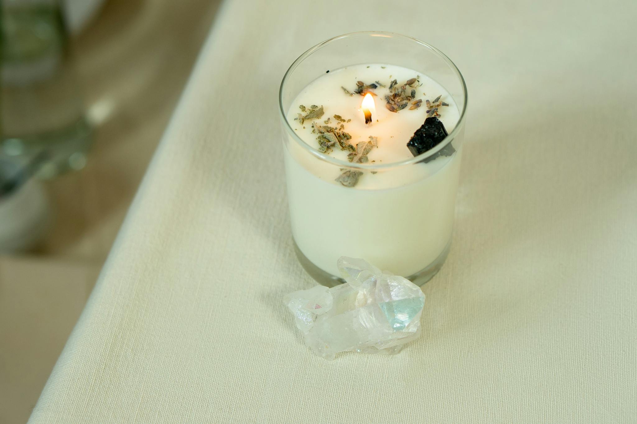 Lit aromatherapy candle with herbs and crystals for relaxation and healing.